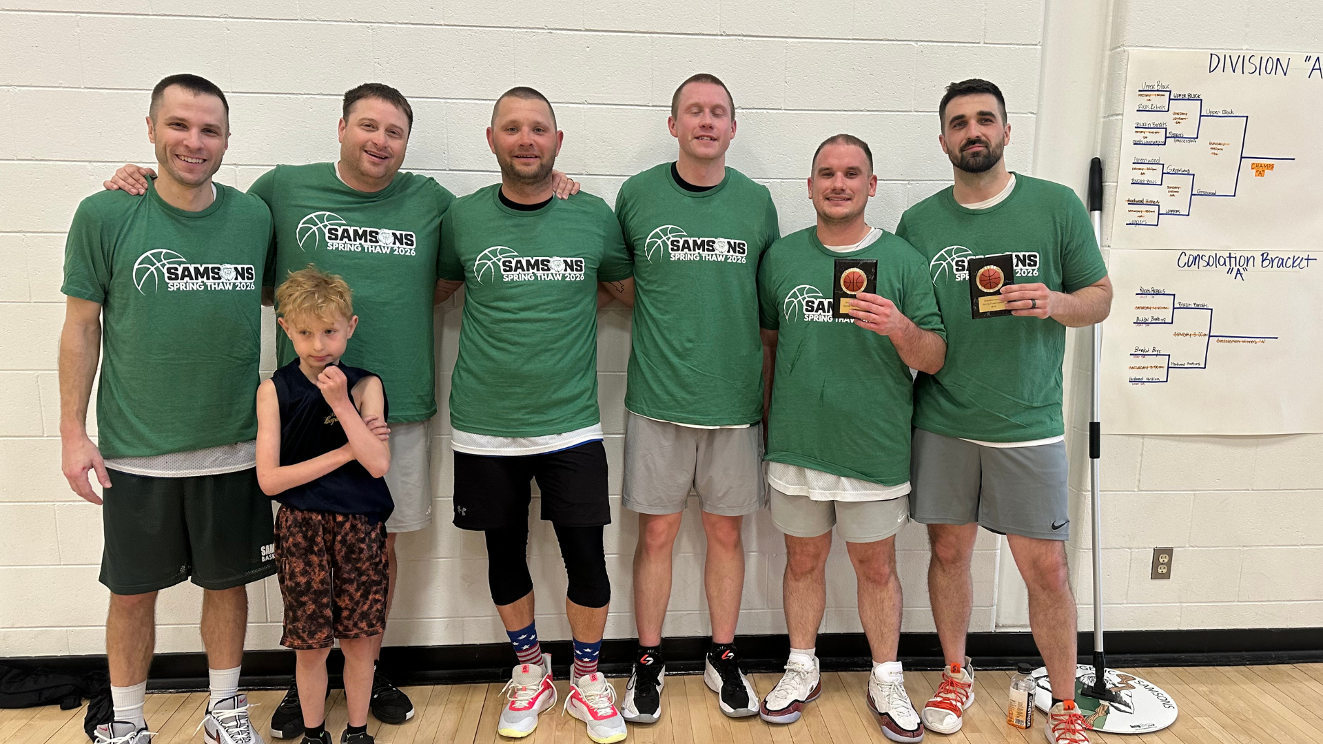 Six men and one boy wearing Spring Thaw tshirts, holding trophies.